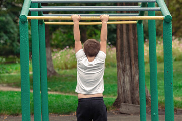 Obraz premium Boy trains on an outdoor sports ground. The boy pull-up on the horizontal bar