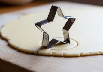 Metal star-shaped cookie cutter on rolled-out sugar dough ready for holiday baking on a wooden board