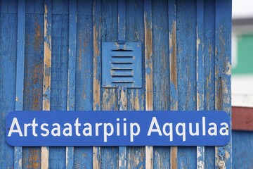 A blue sign inscribed with a Greenlandic street name on a weather-beaten wooden wall, remote Arctic Inuit settlement of Ittoqqortoormiit, Scoresbysund or Scoresby Sund or Greenlandic Kangertittivaq, East Greenland, Greenland