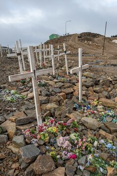 Row of graves with crosses and flowers on a stony cemetery under a grey sky, remote Arctic Inuit settlement Ittoqqortoormiit, Scoresbysund or Scoresby Sund or Greenlandic Kangertittivaq, East Greenland, Greenland