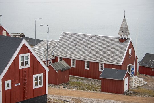Red wooden church with pointed shingle roof surrounded by simple red buildings, secluded Arctic Inuit settlement Ittoqqortoormiit, Scoresbysund or Scoresby Sund or Greenlandic Kangertittivaq, East Greenland, Greenland