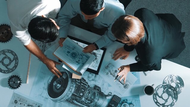 Top down view of skilled engineer working together while looking at jet engine. Aerial view of smart designer or diverse technicians brainstorming while looking at electronic generator. Alimentation. - Powered by Adobe
