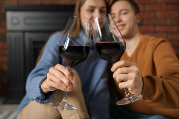 Lovely couple with glasses of wine near fireplace indoors, selective focus