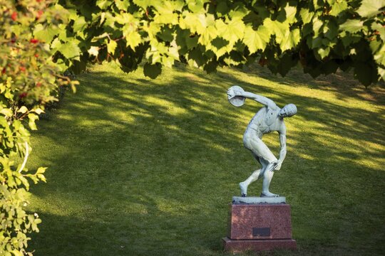 Sculpture of a discus launcher in a green, sunny park area, Botanical Garden or Botanisk Have, University of Copenhagen, Denmark