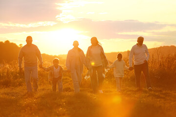 Happy family holding hands in field at sunset