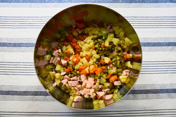 Top-down view of chopped carrots, potatoes, peas, and cucumbers in a metal bowl, ready for Olivier salad. Perfect festive preparation for Christmas or New Year meals.