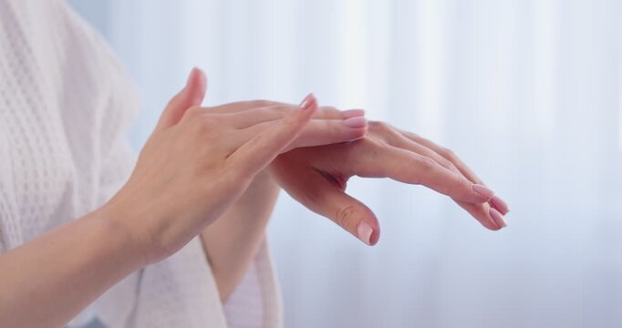Unrecognizable woman in white bathrobe applying cream or body lotion after shower. Closeup hands rubbing in moisturizer cream for soft tender skin and good skin barrier protection. Skin care concept