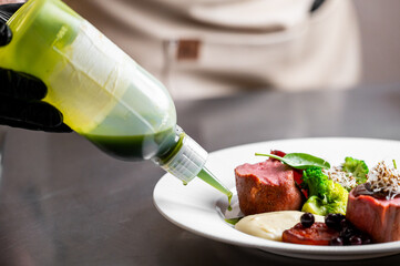 A chef in black gloves carefully garnishes a beautifully plated gourmet dish with a green sauce...