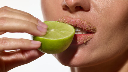 Macro woman lips covered with sugar scrub touching lime slice close-up. Concept of beauty skincare,...