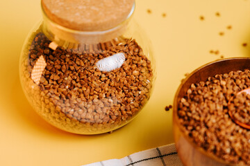 Buckwheat groats in a glass jar and wooden bowl on a yellow background