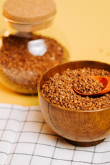 Buckwheat groats in a wooden bowl with a spoon on a yellow background