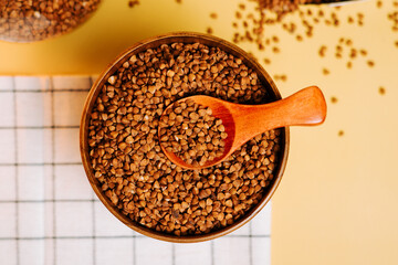 Buckwheat groats in a wooden bowl on a yellow background with a kitchen towel
