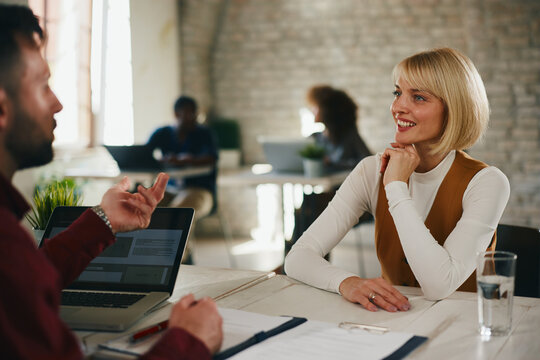 Professional Woman Smiles During Casual Business Meeting At Modern Open-Plan Office With Colleagues And Laptop