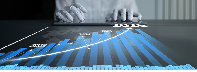 A business professional hands interact with a tablet displaying graphs that represent growth projections from 2023 to 2026, illustrating data analysis and trends. Tessel © InfiniteFlow