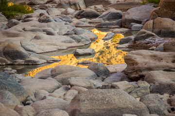 The ethereal golden river of the Fish River canyon. The cliffs of the Fish River Canyon, gold in the late afternoon light, reflecting into the boulder filled river below