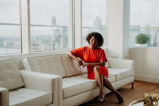 Businesswoman in red dress sitting on sofa in modern office. London view panorama.