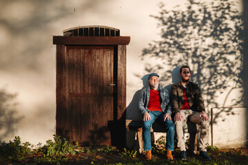 Young man and his grandfather sitting in front of old building.