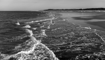 Black-and-white panorama on the beach of the North Sea island of Norderney (Germany) with surf in the Wadden Sea National Park. High-contrast seascape of natural reserve and holiday destination.