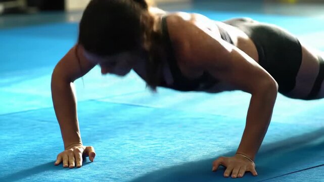 Person performs push-ups on a blue mat in a gym.