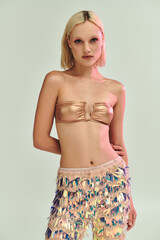 Obraz na płótnie Canvas Blonde young woman showcases stylish party outfit with holographic accents in studio Obraz na płótnie Canvas Blonde young woman showcases stylish party outfit with holographic accents in studio