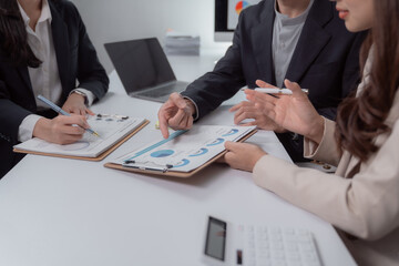 Business professionals collaborating and reviewing financial charts on clipboards during an office meeting, discussing market analysis and developing a strategic plan for growth