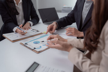 Business professionals collaborating at a table, discussing and analyzing financial graphs and charts on clipboards during a corporate planning meeting in an office environment