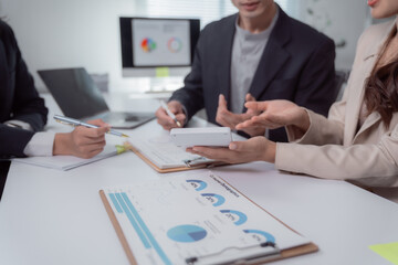 Business professionals collaborating at an office desk, analyzing customer demographics and market data presented on charts while discussing various strategies and new business ideas