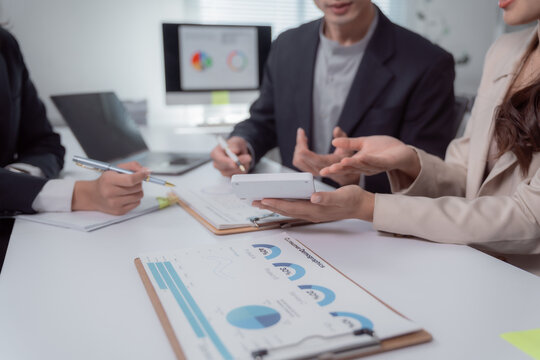 Business professionals collaborating at an office desk, analyzing customer demographics and market data presented on charts while discussing various strategies and new business ideas