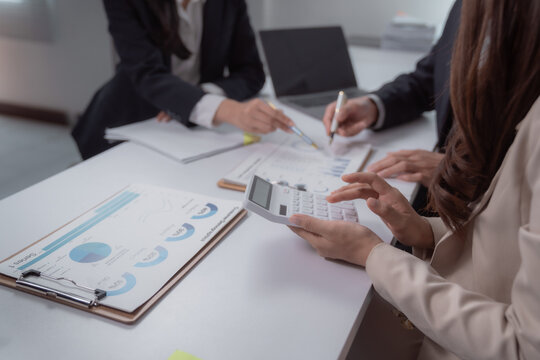 Business team members analyzing financial charts and data on papers while using a calculator, discussing strategy, and preparing for an important meeting in an office setting
