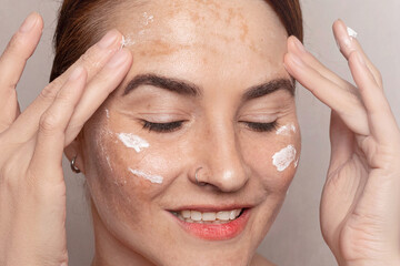 Caucasian woman's face with freckles or age spots, she smears creamon her forehead with her fingers, ncream swatches