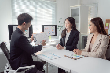 Business team members are analyzing financial data and charts on a clipboard and computer screens during a professional meeting in a modern office, focusing on collaboration and strategic planning