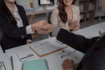 Businesspeople shake hands at a meeting, sealing a partnership over financial reports, calculator and pen on the table, confident colleagues finalizing a contract and strategy