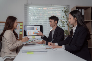 Business professionals collaborating and analyzing financial charts on a computer screen and paper documents, having a productive discussion during a corporate office meeting