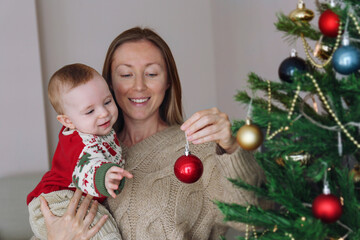 Mom and her newborn decorating a Christmas tree together. Copy space, background.