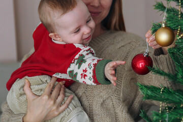 Mom and her newborn decorating a Christmas tree together. Copy space, background.