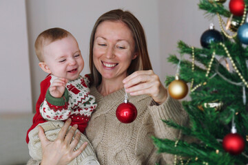 Mom and her newborn decorating a Christmas tree together. Copy space, background.