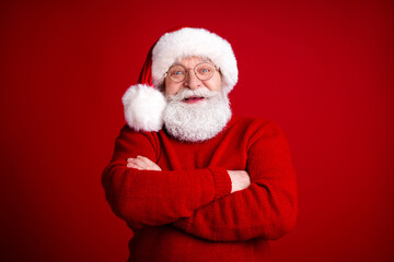 Santa Claus in a cozy red sweater smiles confidently with arms crossed against a bold red background for a festive Christmas themed stock image