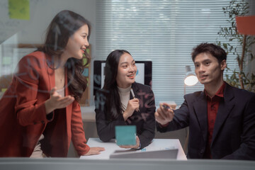 Diverse business team analyzing data and brainstorming ideas on a clear glass whiteboard, developing strategy during an office meeting for successful project execution