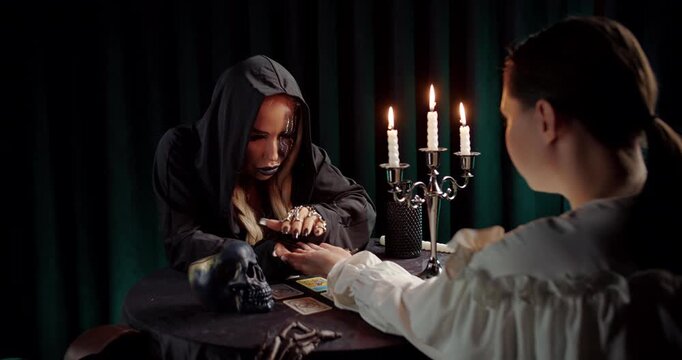 Witch performing palm reading ritual for client under candlelight