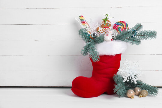 Saint Nicholas day. Red boot with treats and festive decor on floor near white wooden wall. Space for text