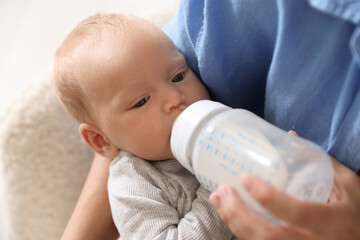 Mother feeding her little baby with bottle at home, closeup