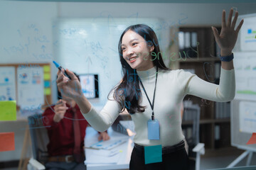 Asian businesswoman actively brainstorming and writing a business strategy on a transparent glass board, smiling while collaborating in a modern office meeting with colleagues