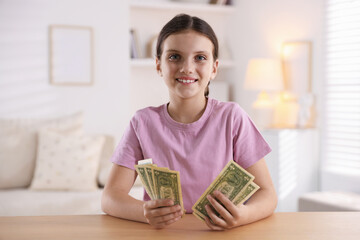 Smiling little girl with dollar banknotes at wooden table indoors. Pocket money and responsibility