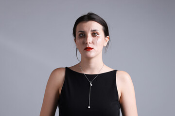 Woman with smeared mascara in dress crying on grey background