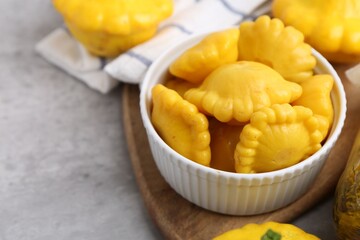 Pickled pattypan squashes in bowl on light grey table, closeup. Space for text