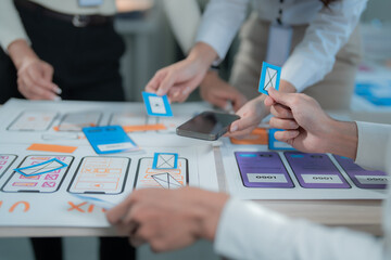 Design team hands actively collaborating, planning, and prototyping mobile application user interfaces on paper wireframes with a smartphone on a meeting table