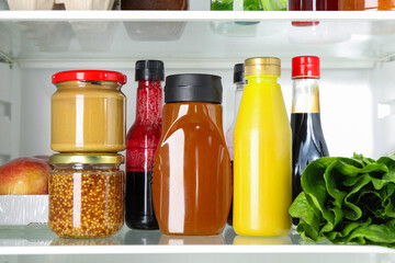 Bottles with different tasty sauces and products in fridge, closeup