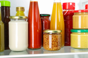 Bottles with different tasty sauces in fridge, closeup