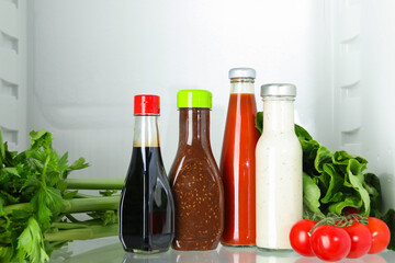 Bottles with different tasty sauces and products in fridge, closeup
