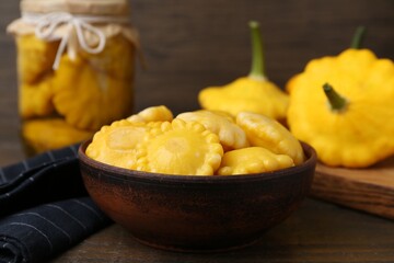 Pickled pattypan squashes in bowl on wooden table, closeup